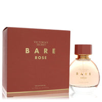 A pink floral fragrance bottle with a white label and gold accents, standing on a wooden surface, labeled "Bare Rose Eau de P