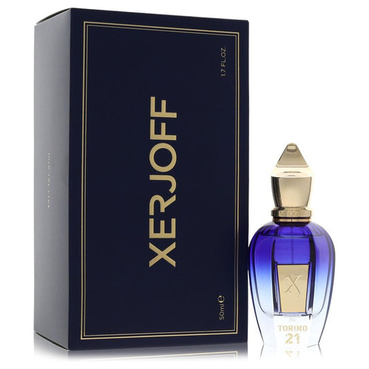 A clear glass bottle with gold accents and a black cap, labeled Xerjoff Torino 21, displayed on a wooden surface by The Fragr
