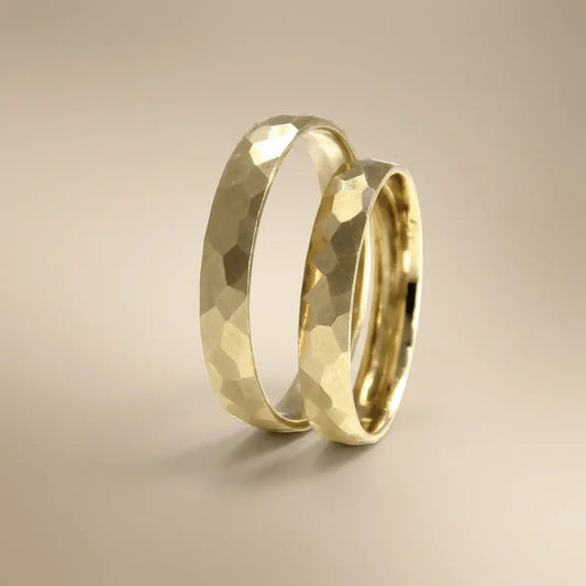 A hammered gold wedding band in 14ct gold with a faceted texture worn on a finger by Majestic Jewellery.